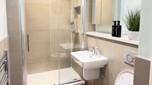 A modern bathroom with a glass-enclosed shower, a white sink, and a mirror above it. - Airport Stays - Deluxe Studio London Heathrow (Hayes)