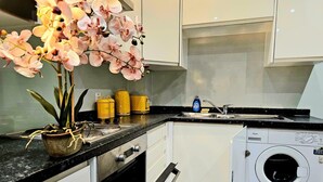 A compact kitchen with a washing machine, a sink, and a potted orchid. - Airport Stays - Deluxe Studio London Heathrow (Hayes)