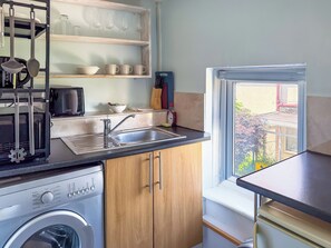 Eine kleine Küche mit Waschmaschine, Spüle und einem Fenster mit Blick nach draußen.