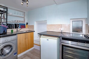 Eine kompakte Küche mit Waschmaschine, kleinem Kühlschrank, Mikrowelle und Herd.