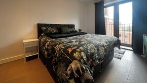 Une chambre avec un grand lit, une table de chevet et une vue sur un immeuble par la fenêtre.