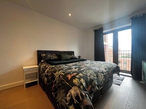 A bedroom with a large bed, a nightstand, and a view of a building through a window. - Grosvenor Rd Studio - Sleeps 4, Pet Friendly, Wifi (St Albans)