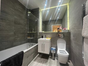 A modern bathroom with a glass-enclosed shower, a white toilet, and a vanity with a mirror. - Grosvenor Rd Studio - Sleeps 4, Pet Friendly, Wifi (St Albans)