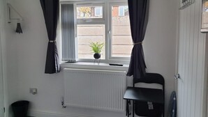 Una habitación con ventana, radiador, planta en maceta, una silla y un protector de radiador en el suelo.