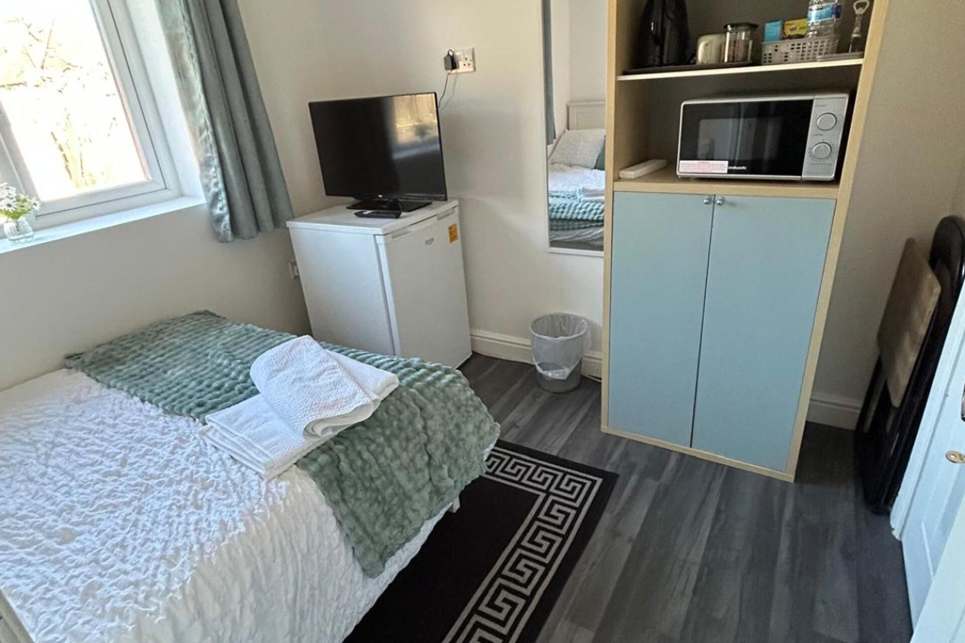Quarto com cama, televisão, micro-ondas, guarda-roupa e um pequeno cesto de lixo.
