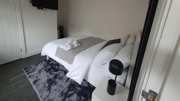 Un dormitorio moderno con cama, televisor de pantalla plana en la pared y una mesita de noche.