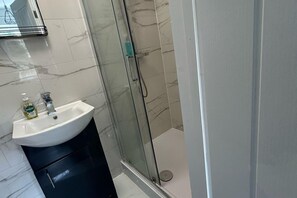 A bathroom with a white sink, a glass shower enclosure, and a marble-tiled wall. - Private Room, Sleeps 2 With Ensuite & Parking (Birmingham)