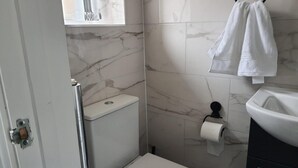 Un baño con inodoro, lavamanos, toallero y dispensador de papel higiénico.