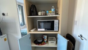 Una kitchenette compacta con microondas, un refrigerador pequeño y una alacena con artículos de cocina esenciales.