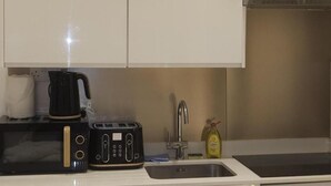 Keittiössä on mikroaaltouuni, leivänpaahdin ja kahvinkeitin työtasolla, pesuallas sekä pullo astianpesuainetta.