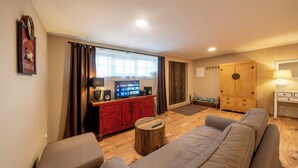 Una sala de estar con un sofá, una mesa de centro de madera, un televisor sobre un mueble rojo y un armario de madera.