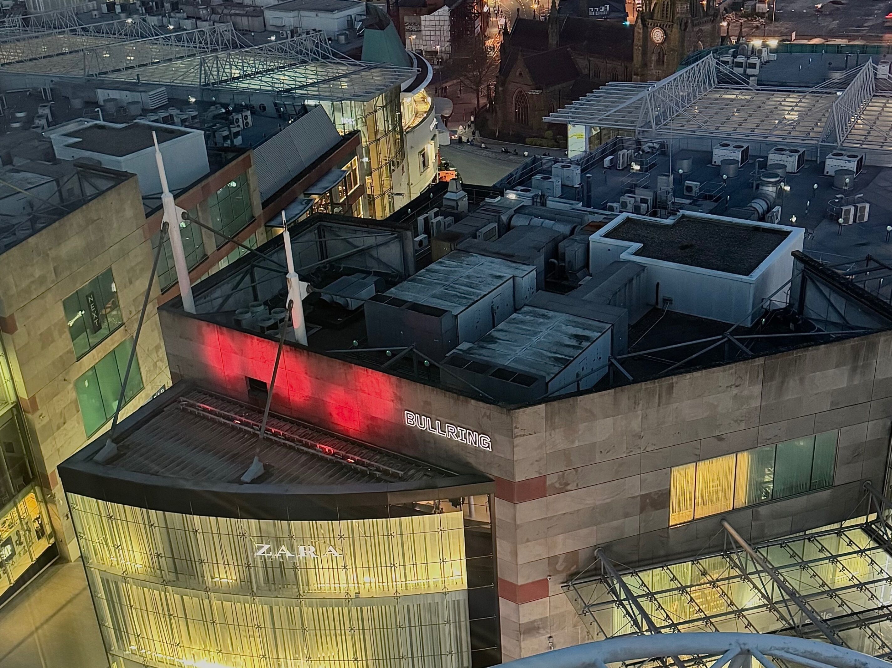 Ein mehrstöckiges Gebäude mit einem Zara-Geschäft im Erdgeschoss, einem Bullring-Schild in den oberen Etagen und verschiedenen Gebäudestrukturen auf dem Dach.