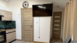 Una habitación pequeña con cama, televisión, kitchenette y una puerta que da a otra habitación.