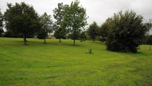 Un campo cubierto de césped con árboles y una pequeña construcción.