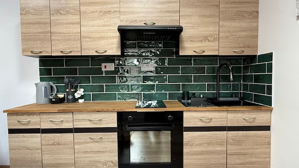 Una cocina moderna con armarios de madera, campana extractora negra, azulejos de salpicadero verdes y lavavajillas.
