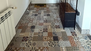 Un pasillo con piso estampado, una puerta blanca con paneles de vidrio y un estante metálico negro con una pequeña planta.