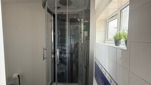 Un box de ducha con puerta de vidrio, una ventana arriba y una maceta sobre el alféizar.