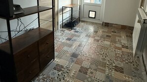 Una habitación con suelo estampado, un armario de madera, una estantería de metal y una puerta que da al exterior.