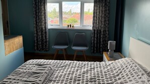 Un dormitorio con cama, dos sillas, una ventana con cortinas y vistas a casas.