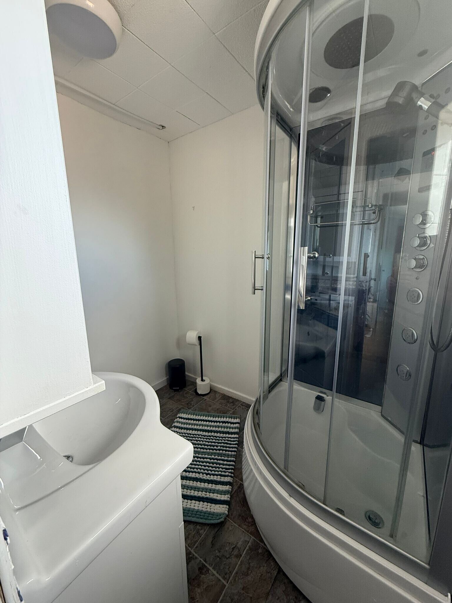 A bathroom with a glass-enclosed shower, a white sink, and a striped bath mat.