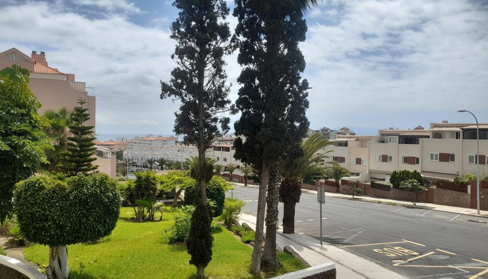 A residential area with a road, greenery, and buildings.