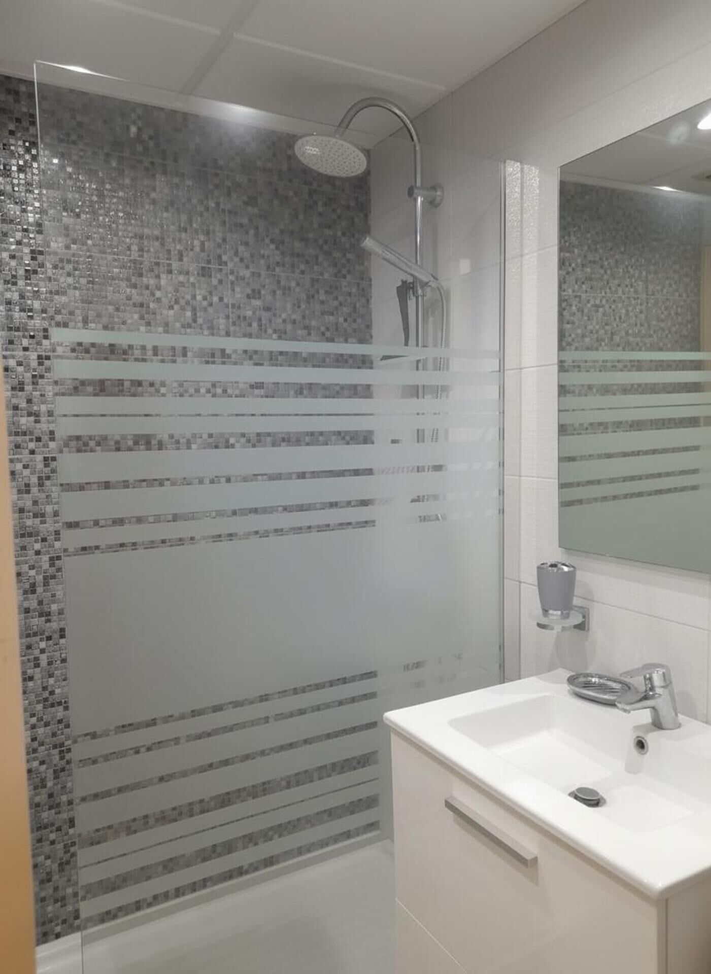 Une salle de bain moderne avec une douche à parois de verre, un lavabo blanc et un miroir.