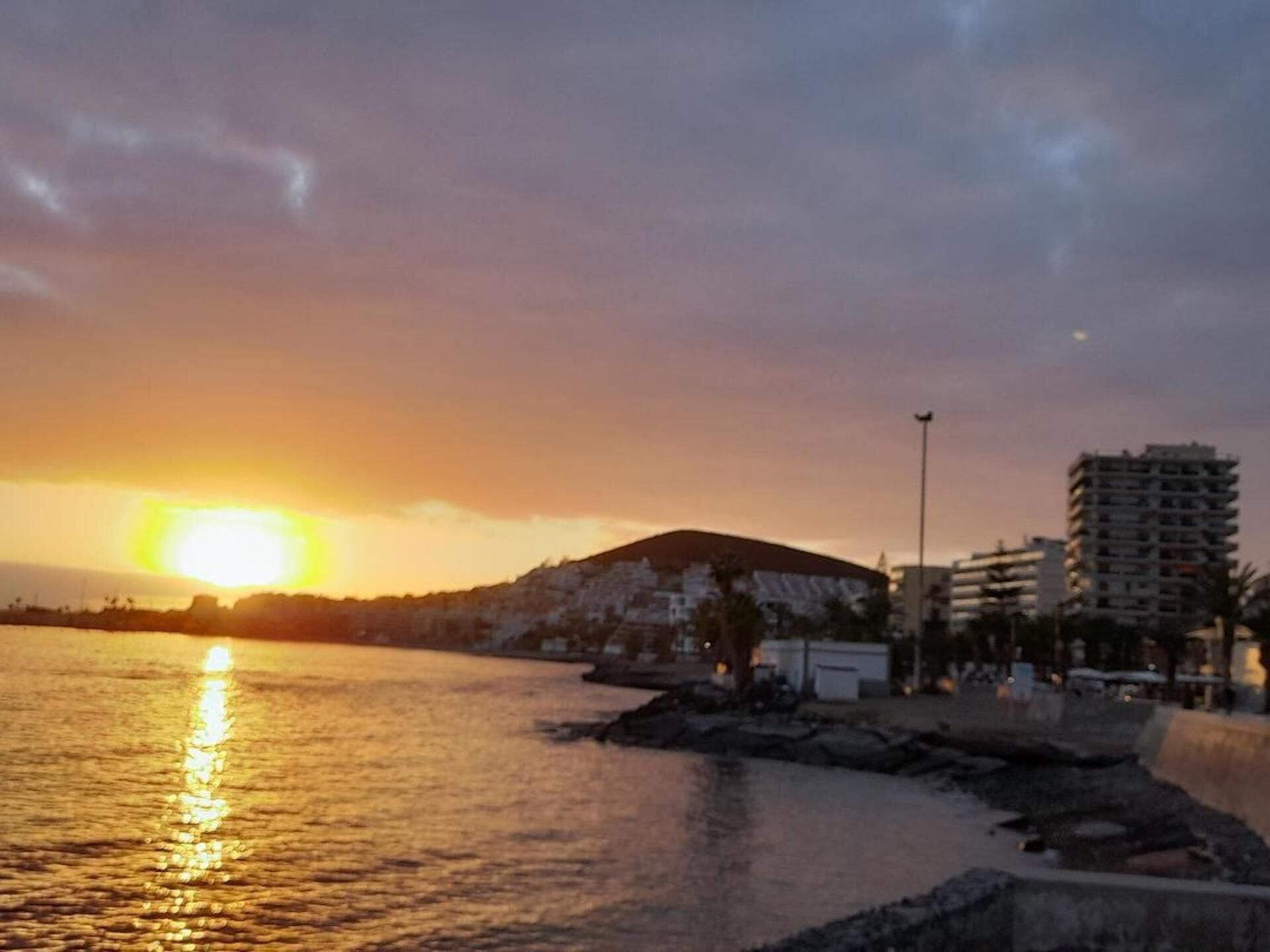 Un atardecer sobre una masa de agua con edificios y una colina al fondo.