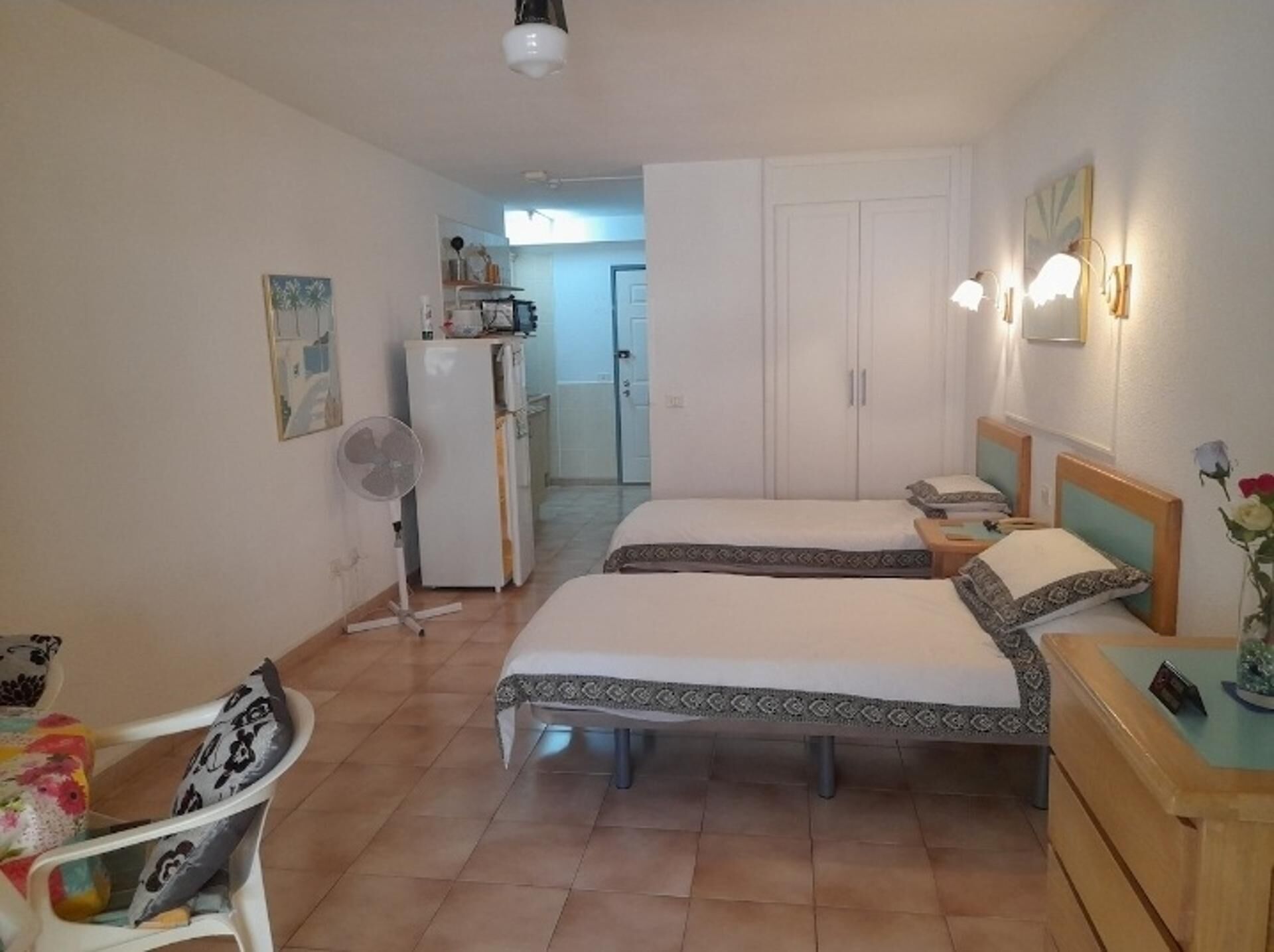 A bedroom with two beds, a desk, a chair, a fan, and a wardrobe.