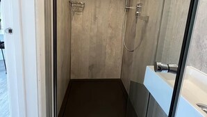 En bruseniche med glasvægge, et kontrolpanel, brusehoved og et håndspejl.