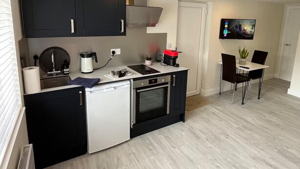 Et moderne køkken med indbygget ovn, kaffemaskine og spiseplads med bord og stole.