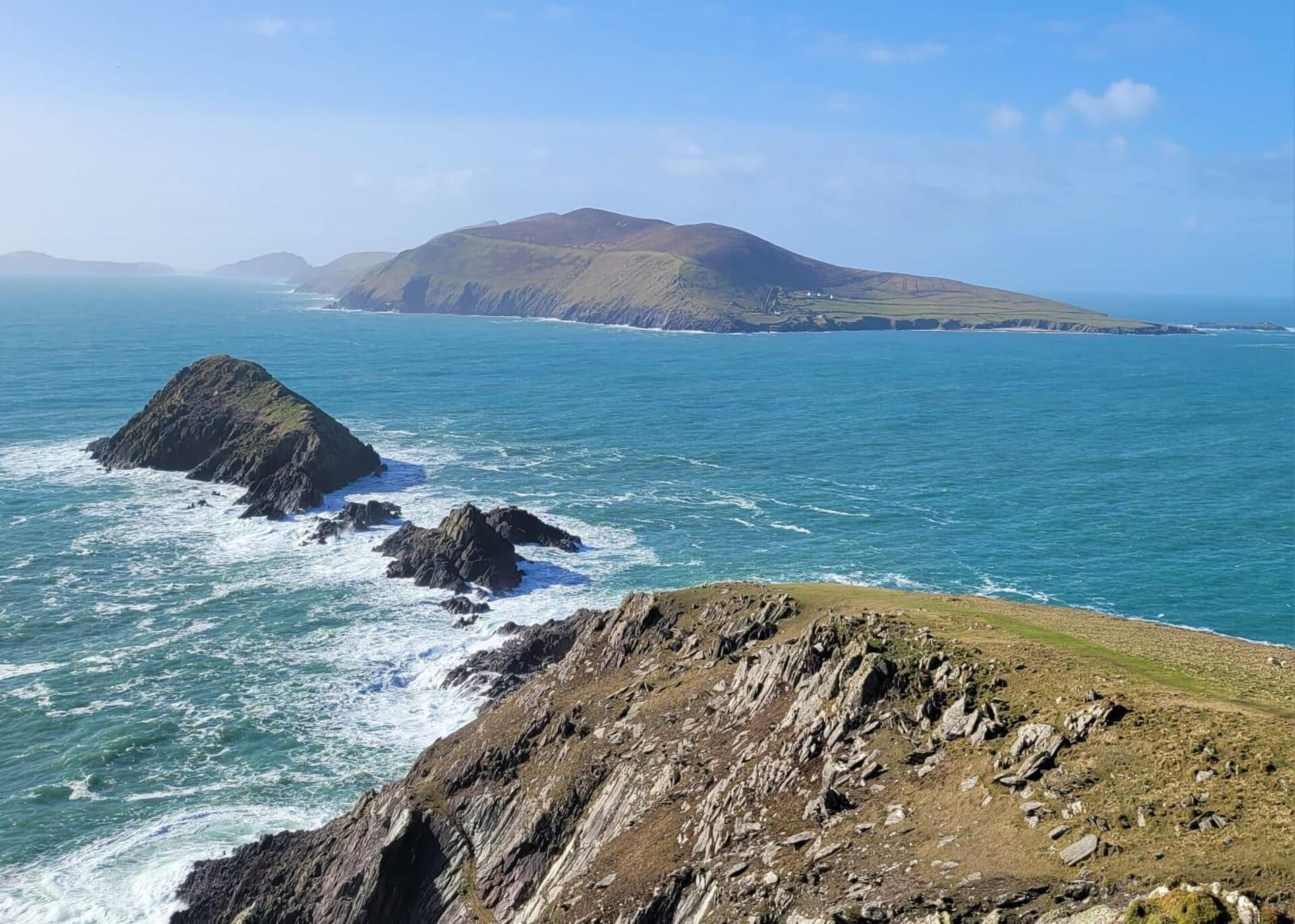 A coastal landscape with rocky terrain and a distant mountain.