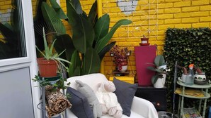 Une pièce avec une chaise blanche, une grande plante en pot, un meuble rouge et un mur en briques jaunes.