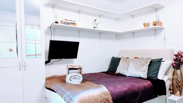Une chambre avec un lit, une télévision, une étagère remplie de livres et une fenêtre.