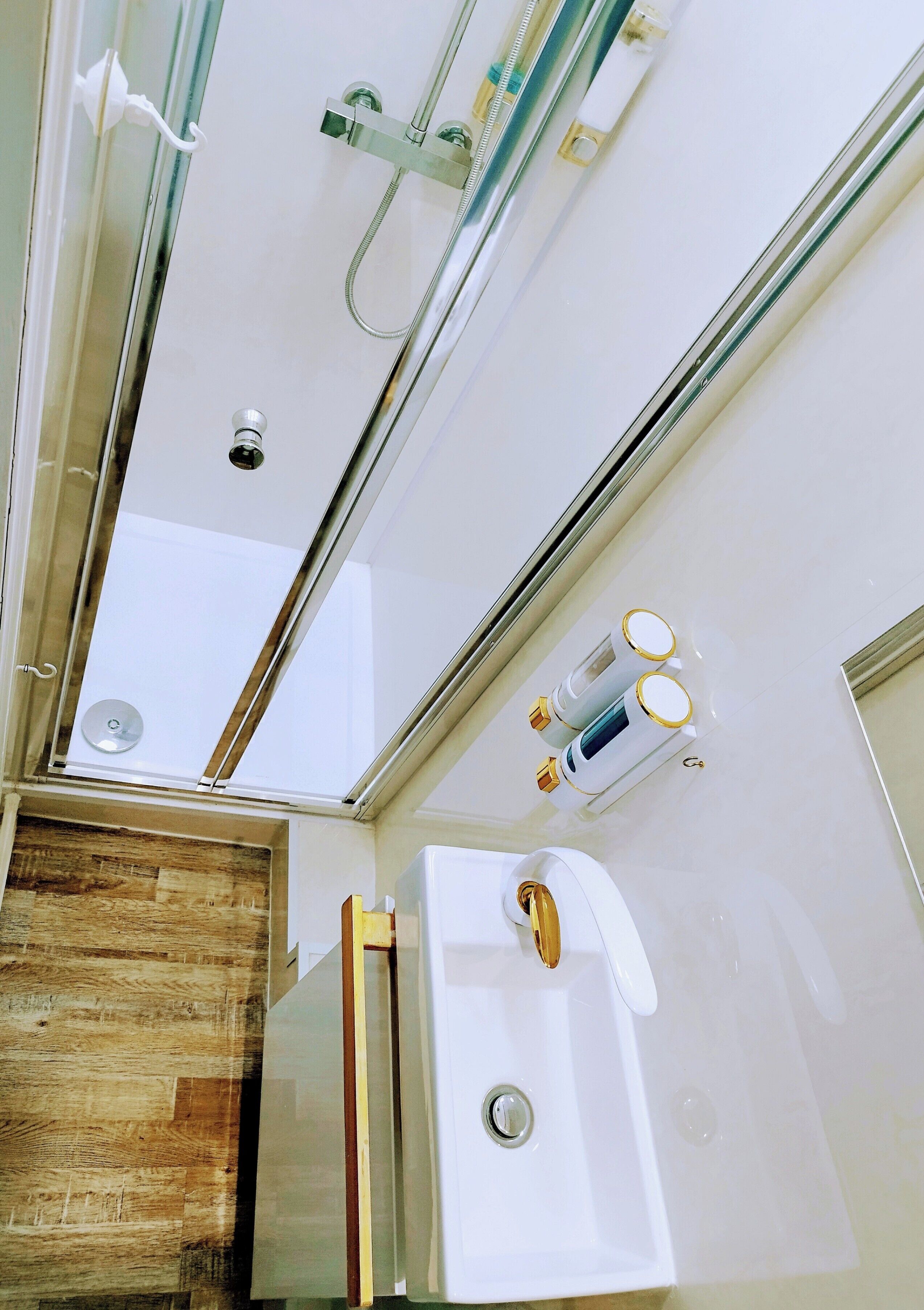 A bathroom with a glass shower enclosure, a white sink with gold fixtures, and a wooden accent wall.