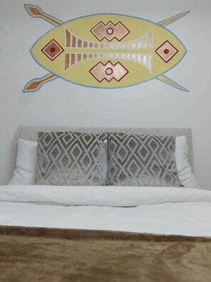 Ein Bett mit gemusterten Kissen und einer Wanddekoration darüber.