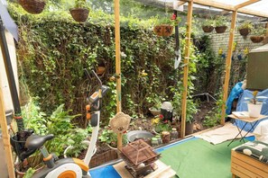 Ein Garten mit verschiedenen Pflanzen, einem kleinen Teich und Gartenwerkzeugen.
