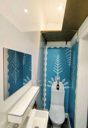 Ein Badezimmer mit einer weißen Toilette, einem weißen Waschbecken und einer blauen Wand mit Blätermotiv.