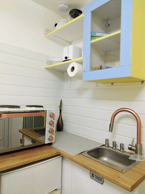 A compact kitchen with a sink, a stove, and a cabinet with a yellow door. - Cozy Studio Zulu, Central London (London)