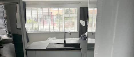 A modern kitchen with a built-in sink, a window with blinds, and a ceiling light fixture.