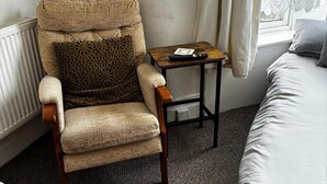 A chair with a patterned cushion, a small wooden table with a remote control, and a bed with a pillow. - Studio Sleeps 1 - Pets Welcome -free Parking (Blackpool)
