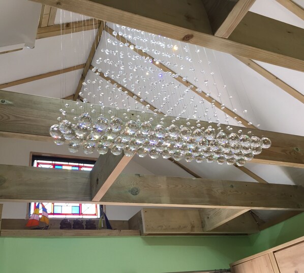 A room with exposed wooden beams, a hanging chandelier with multiple clear crystal orbs, and a window with colorful stained glass. - Seaside Retreat Studio in Hayling Island (Hayling Island)