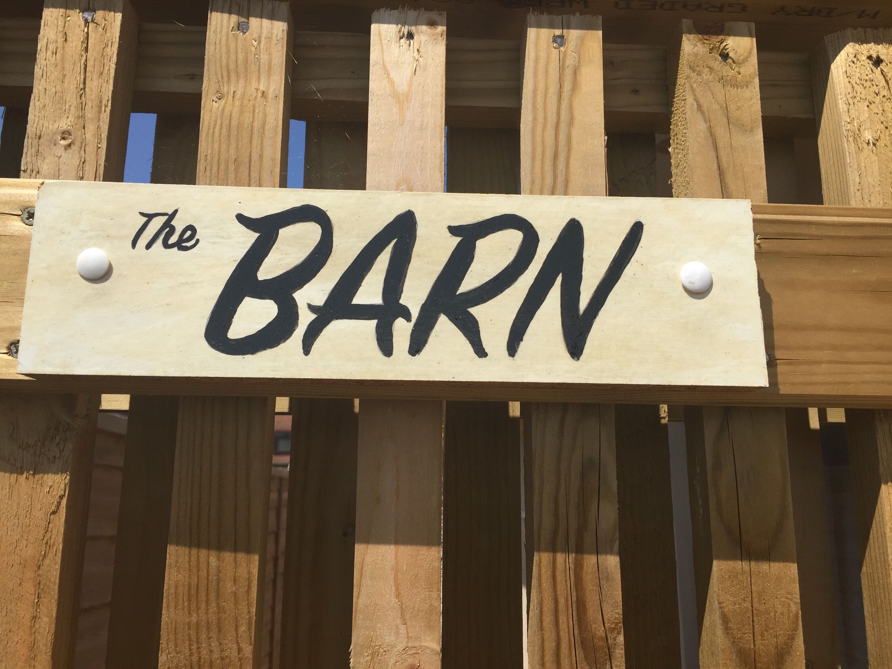 A wooden sign with the text "The BARN" mounted on a wooden fence.