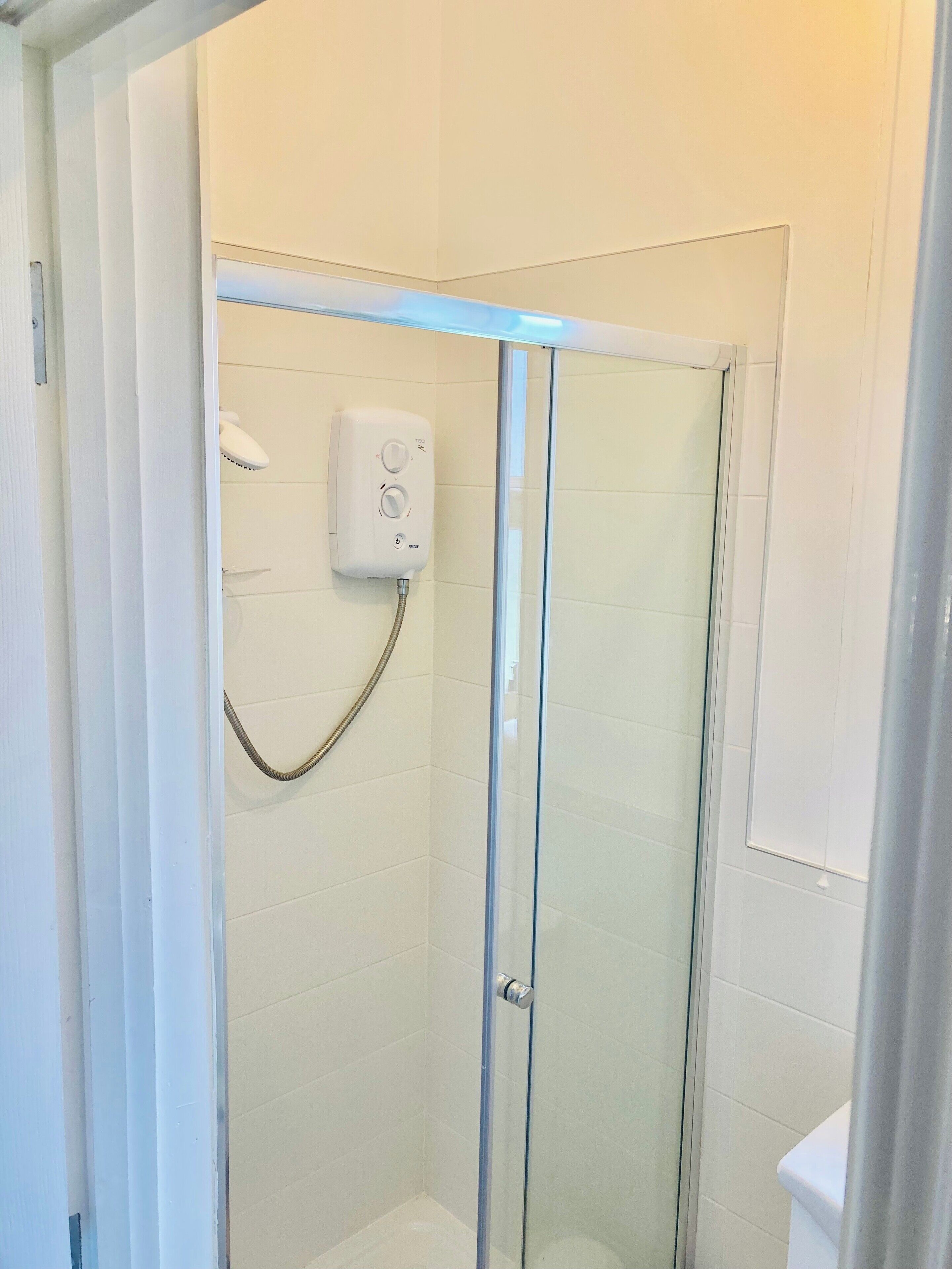 Un box de ducha con paredes de vidrio, un cabezal de ducha de mano y un panel de control.