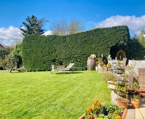 Ein gepflegter Garten mit Hecke, Gartenmöbeln und diversen Blumentöpfen.