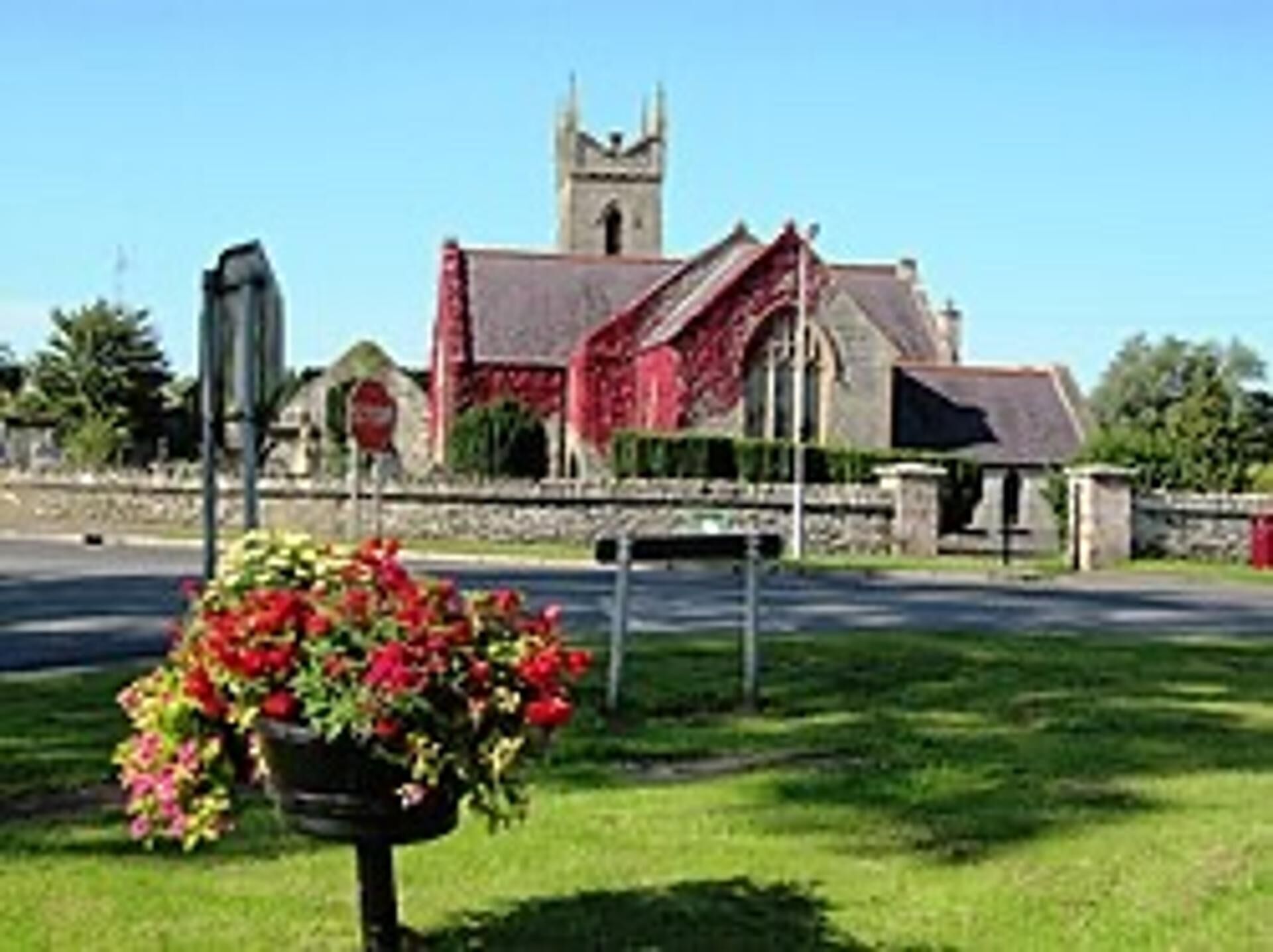 A church with a tower, a road in front, and a flower bed.