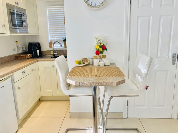 Una cocina moderna con microondas integrado, cafetera y un lavabo. Hay una mesa de comedor con sillas y un florero.