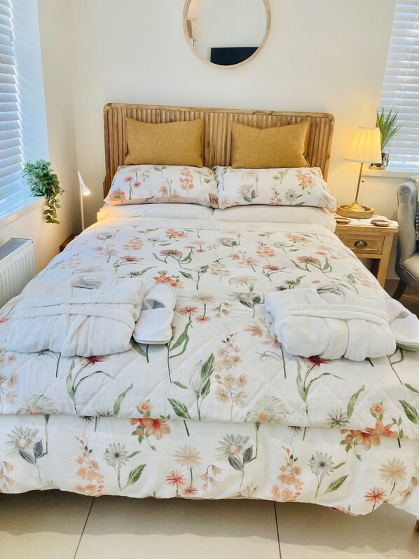 Un lit bien fait, avec une literie à motifs floraux, un miroir rond au-dessus et une lampe de chevet.