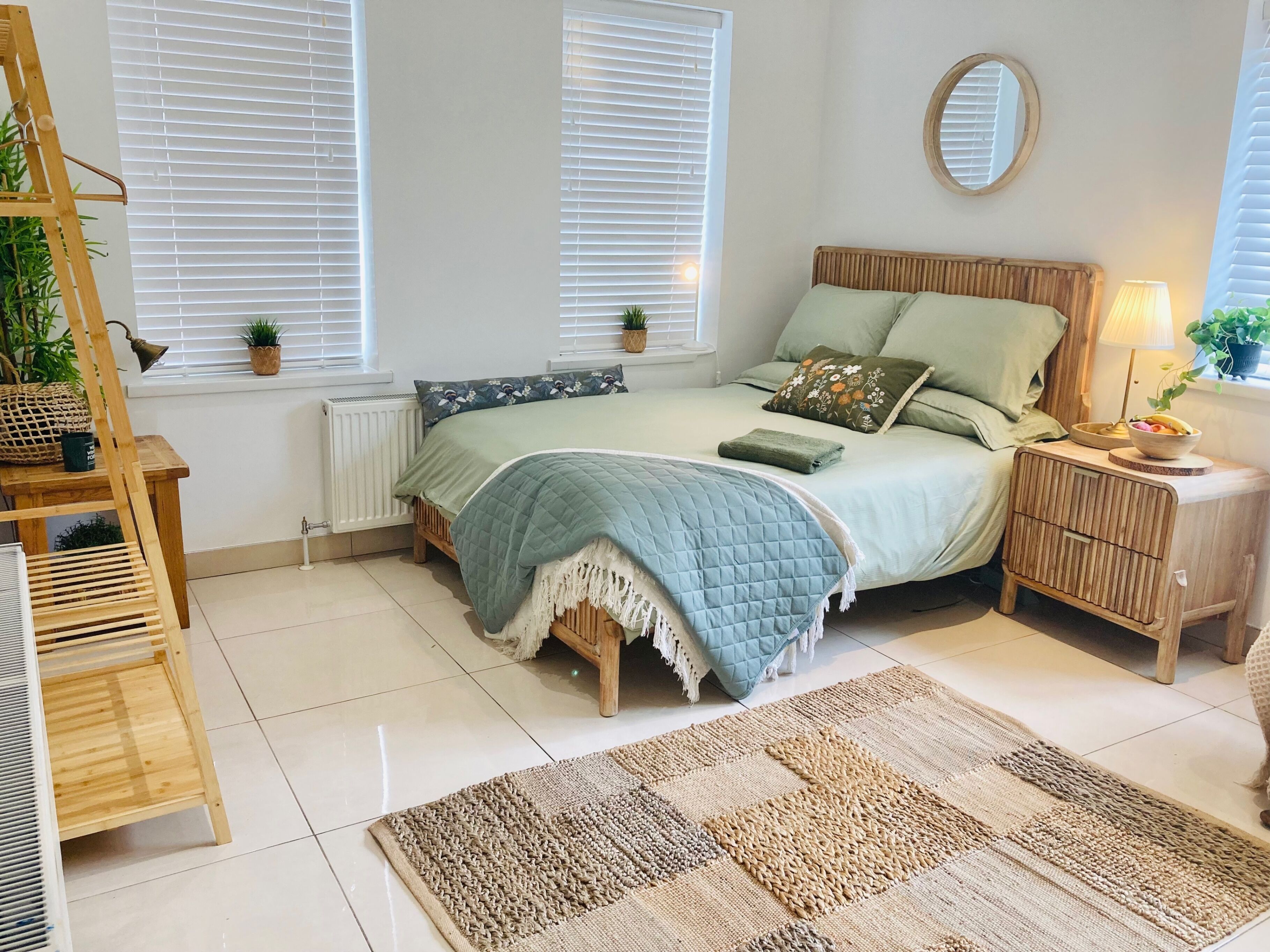 Un dormitorio con cama, mesitas de noche, una escalera de madera, un radiador y una ventana con persianas.