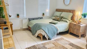 Un dormitorio con cama, mesitas de noche, una escalera de madera, un radiador y una ventana con persianas.