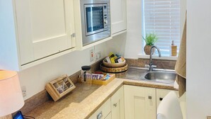Una cocina con armarios blancos, horno empotrado, un lavabo y una ventana con persianas.